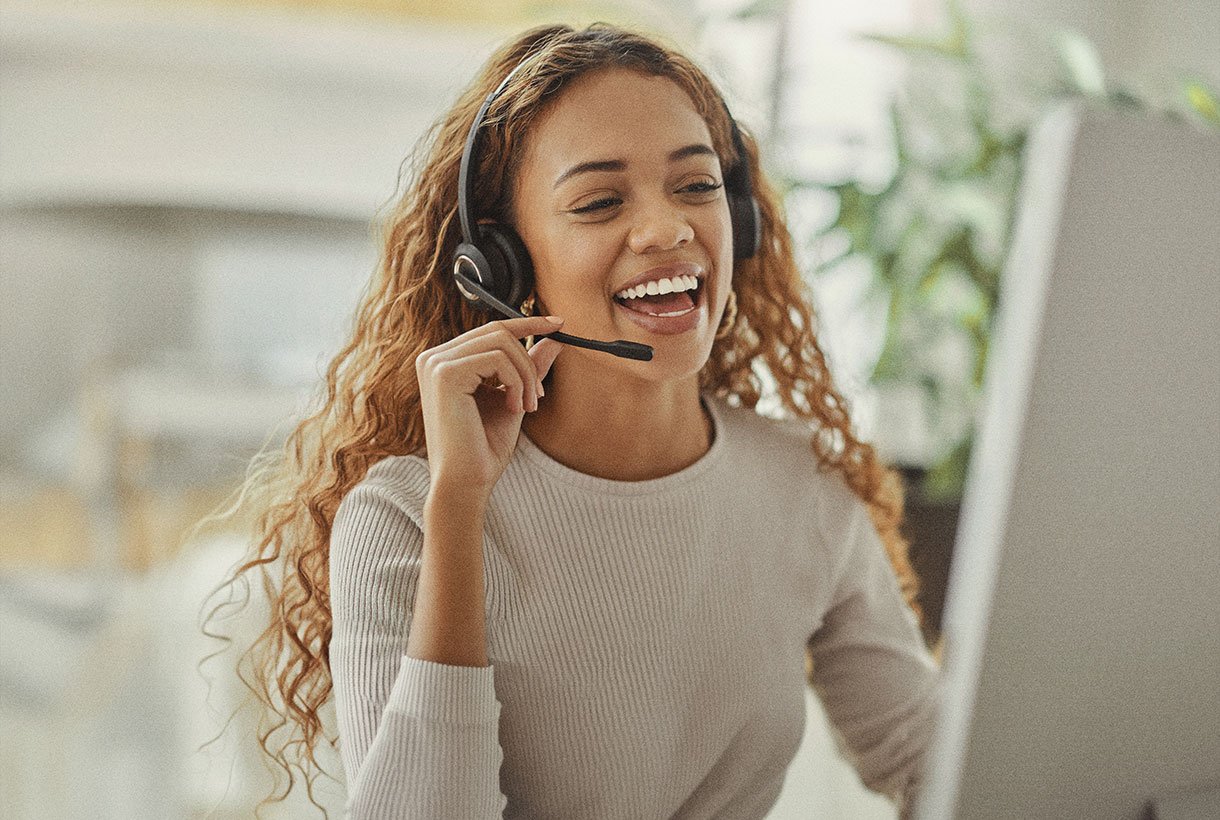A person smiling at a computer while wearing a headset