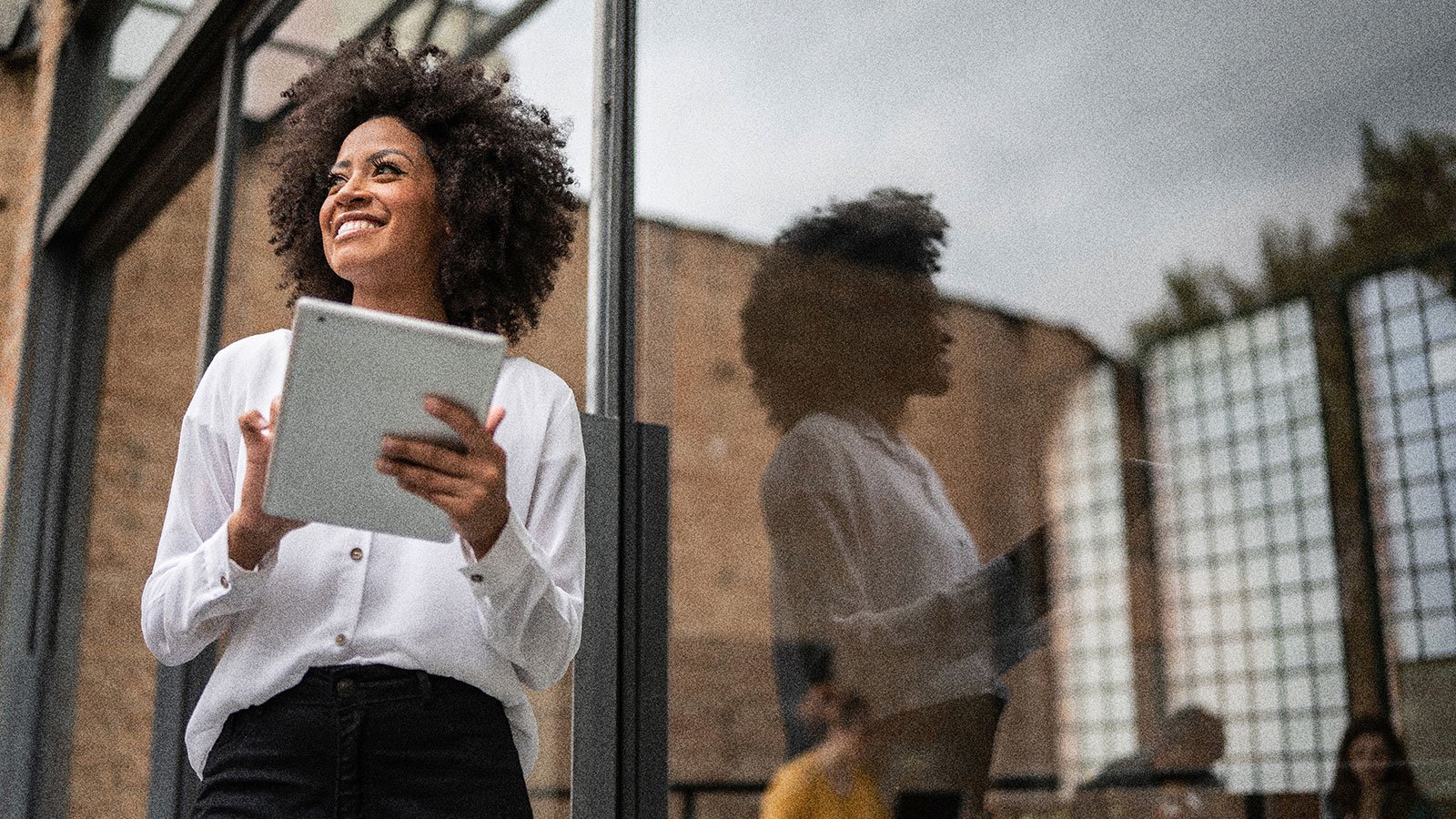 A person smiling outdoors while holding a tablet