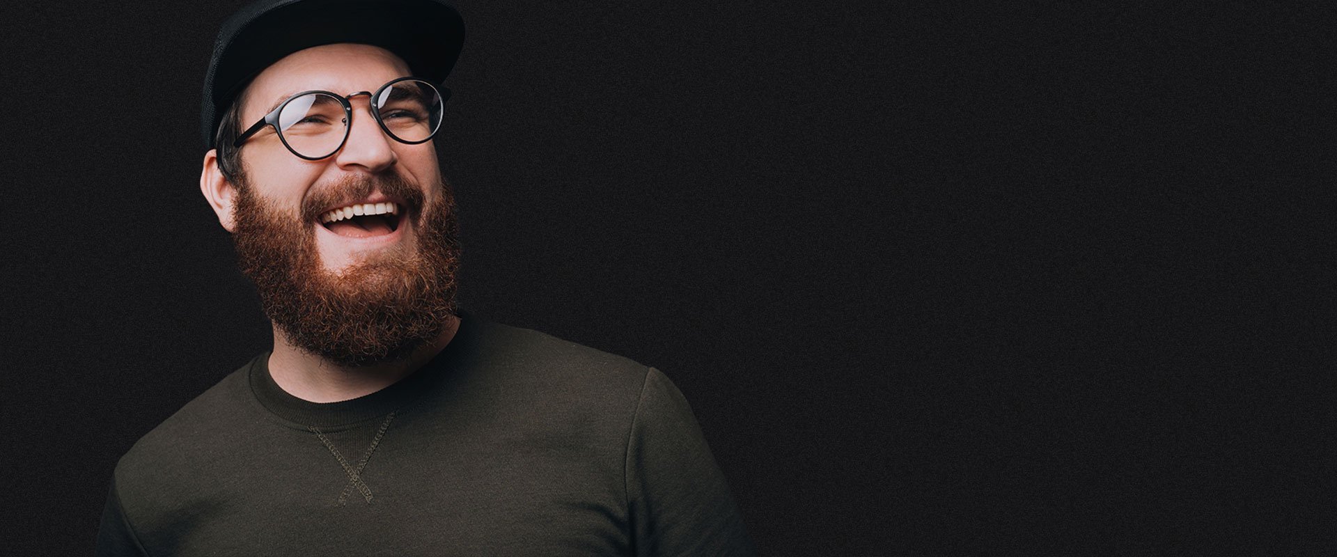 A person with glasses and a cap laughing warmly